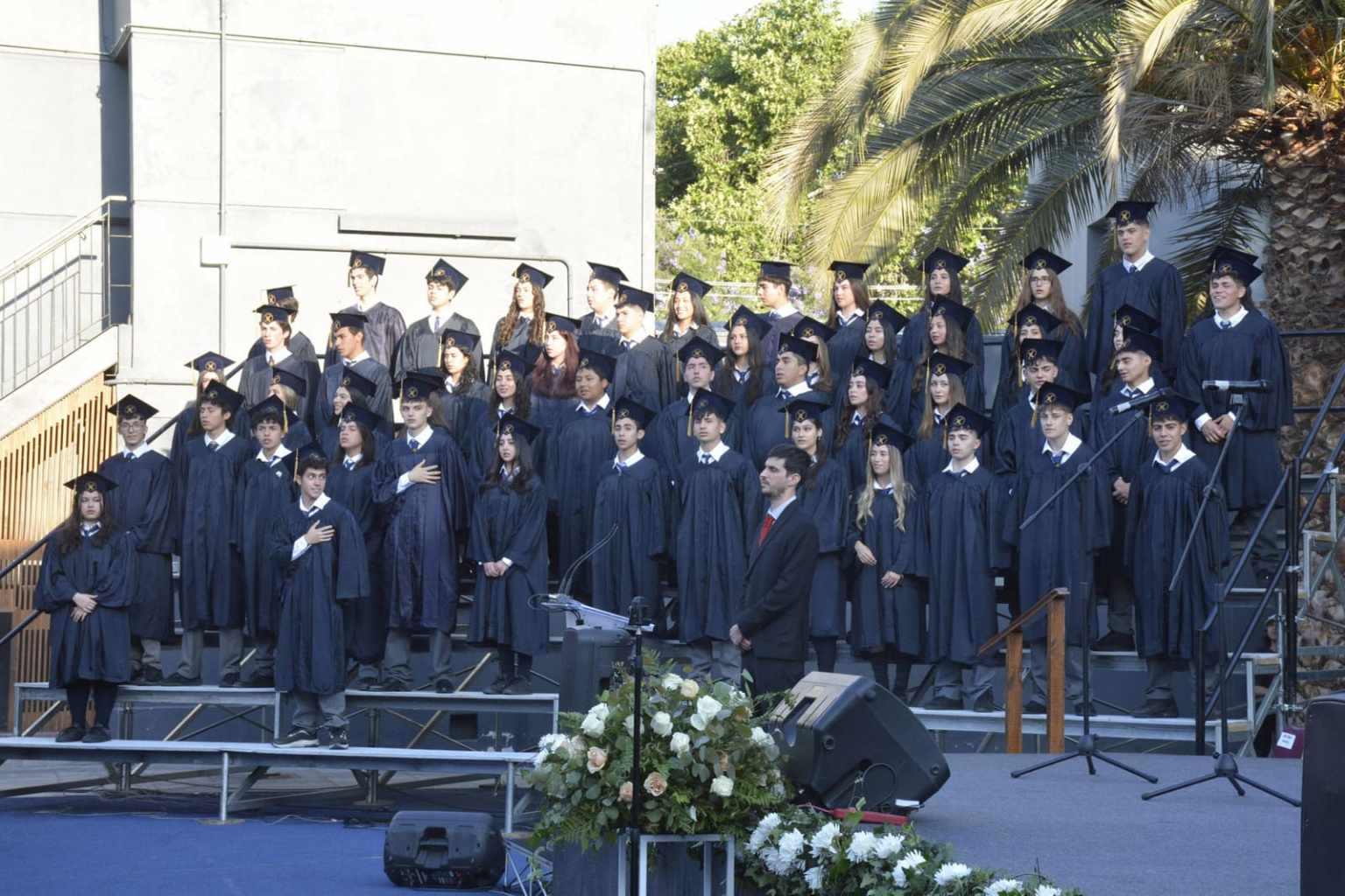Graduados del Colegio TEI con toga y birrete en el escenario de la ceremonia
