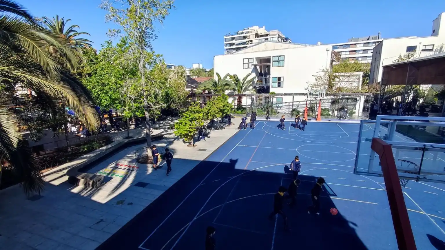 Estudiantes del Colegio TEI en recreo en el patio central, junto a la cancha azul y palmeras