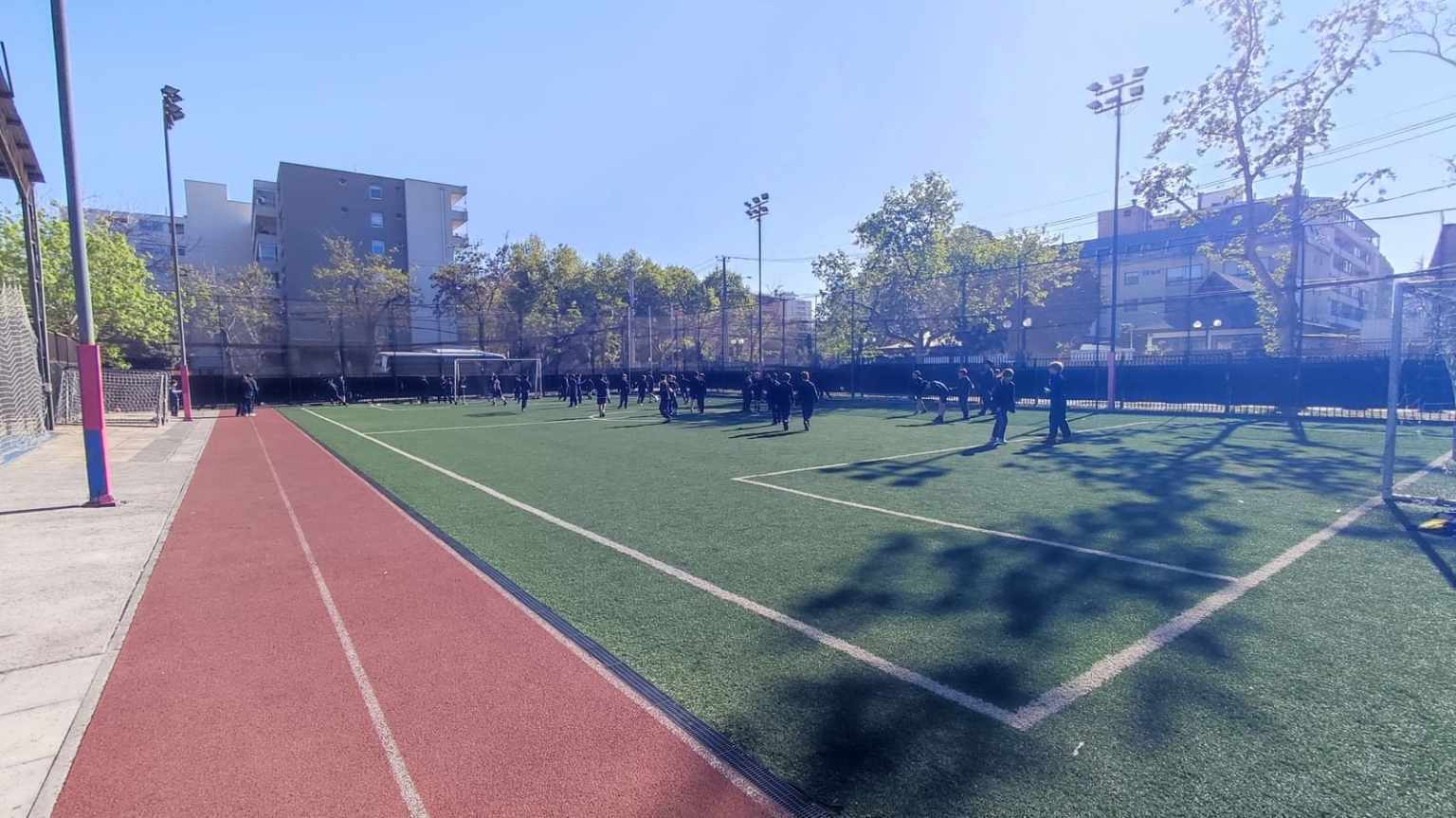 Cancha de fútbol de pasto sintético y pista atlética del Colegio TEI con estudiantes