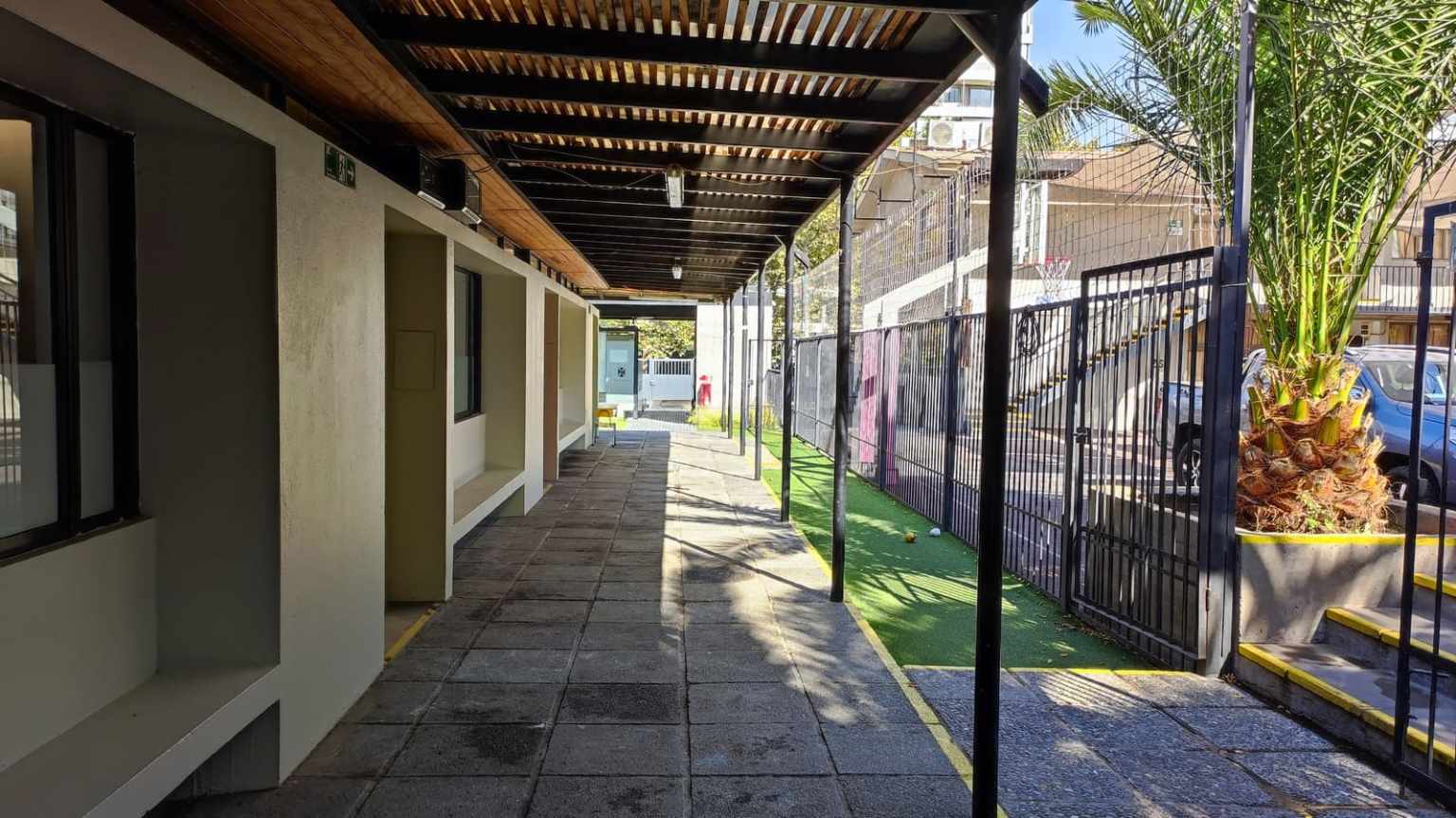 Pasillo techado junto a las salas de Junior School del Colegio TEI, con palmeras y jardín