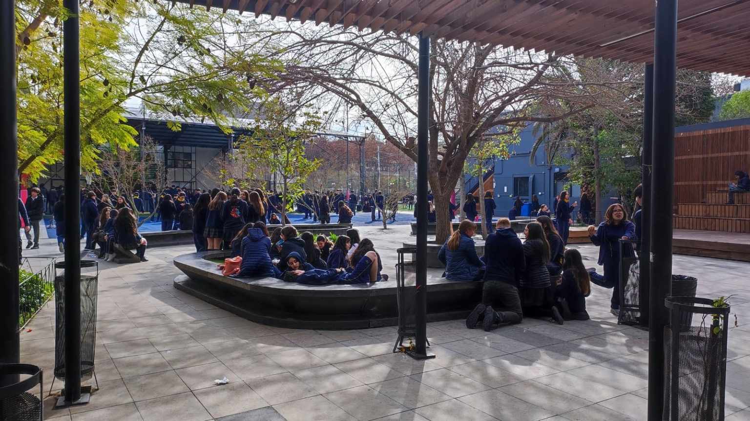 Estudiantes del Colegio TEI sentados en las bancas del patio arbolado