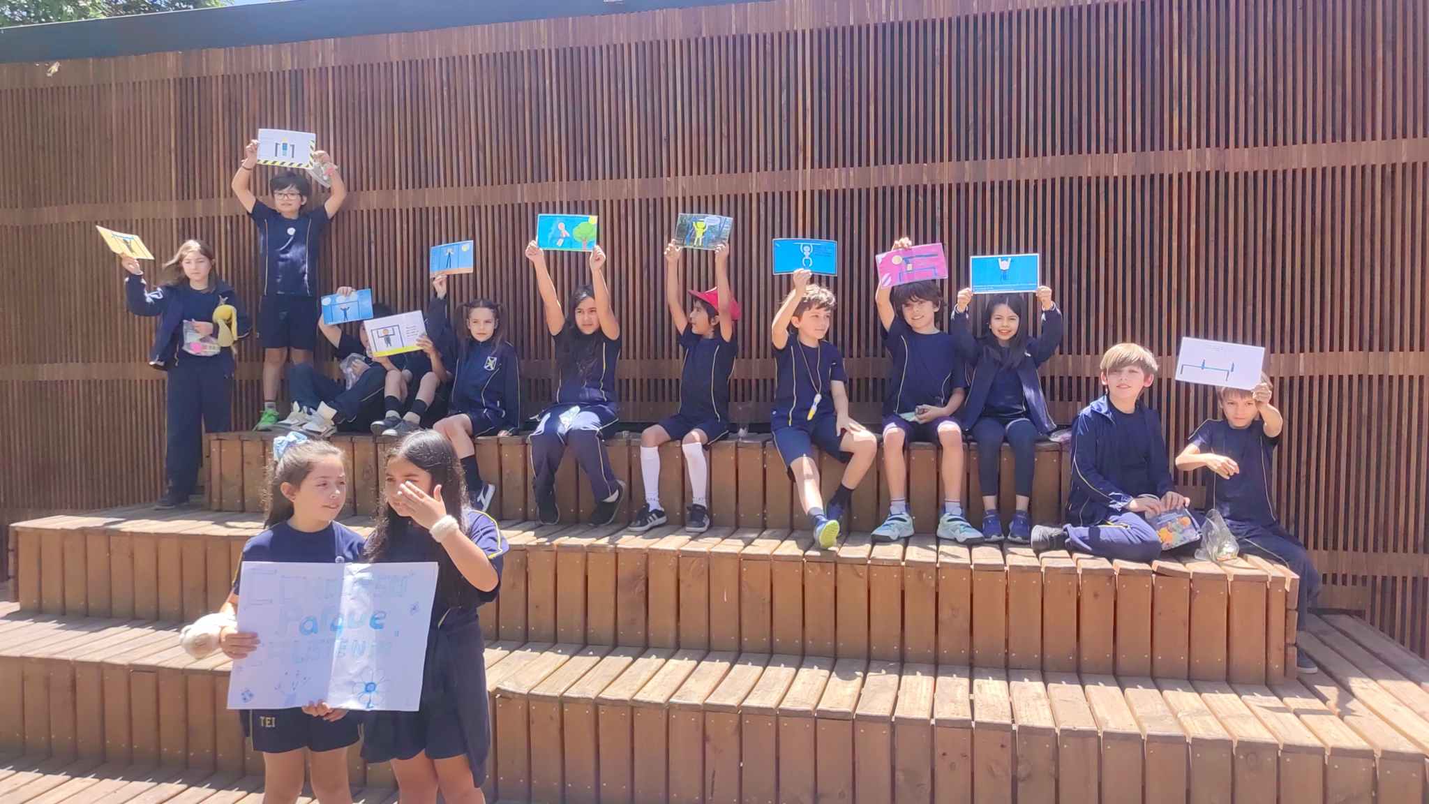Estudiantes de Junior School del Colegio TEI mostrando sus dibujos en unas graderías de madera