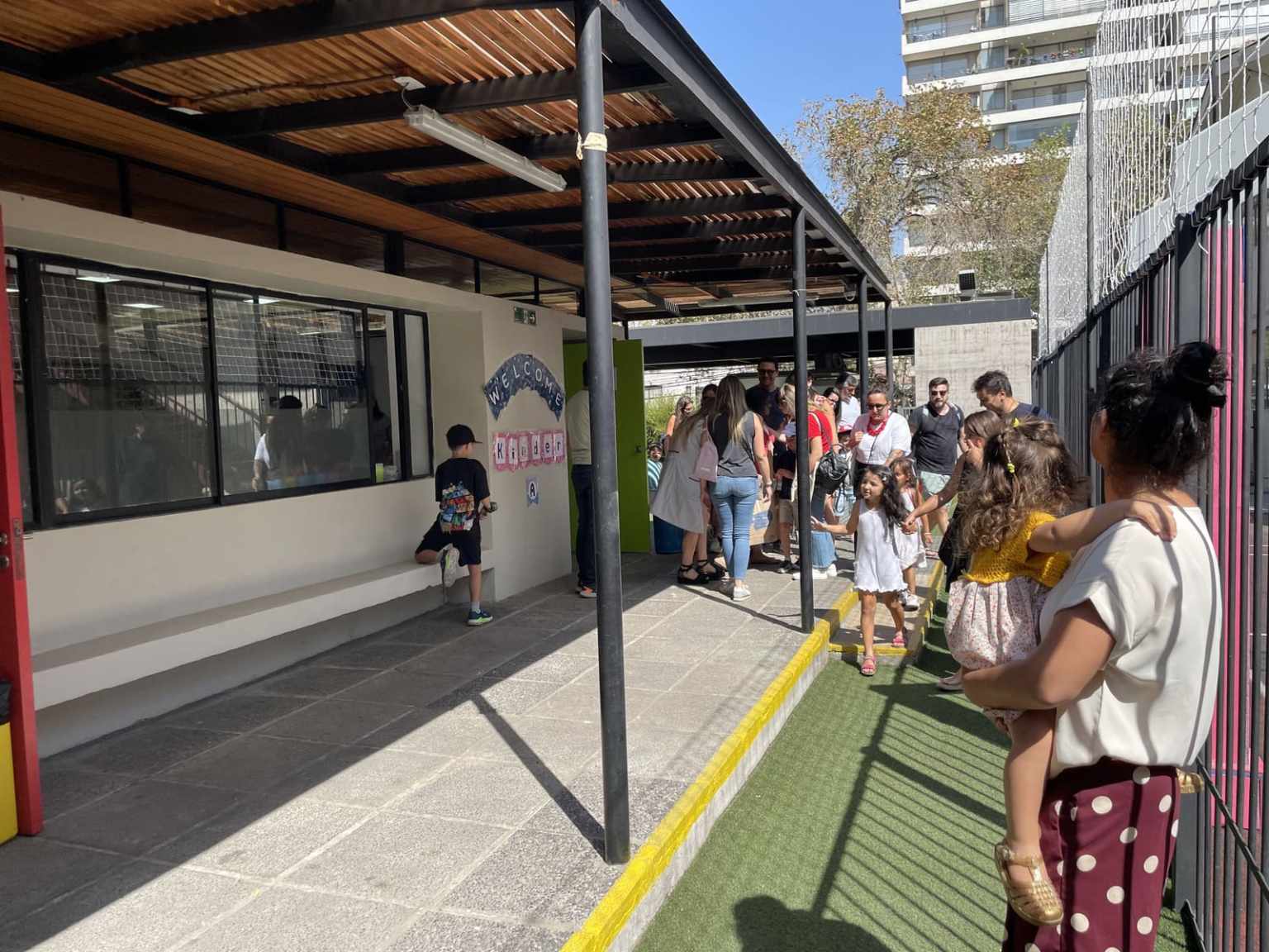 Familias con niños pequeños del Colegio TEI en un pasillo techado del colegio