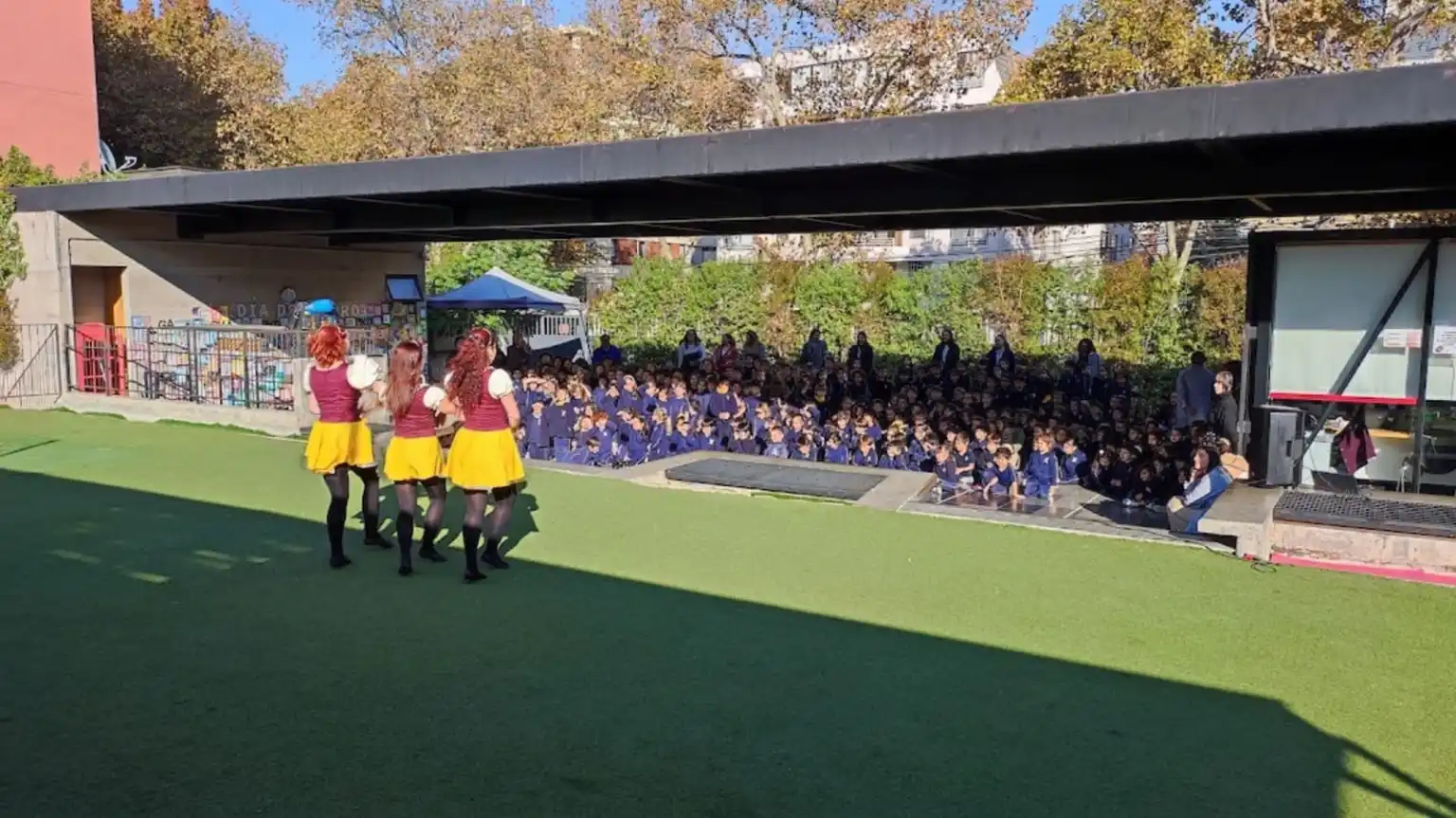 Estudiantes del Colegio TEI sentados bajo un techo viendo una presentación de baile en el pasto